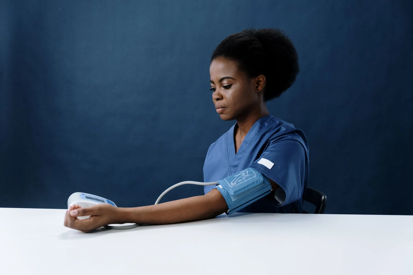 A nurse in blue scrubs taking a blood pressure reading
